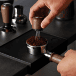 Zwarte koffiemolen met hand die gemalen koffiebonen maalt, vers en aromatisch, voor koffie en thee liefhebbers, bij Koffie Thee Lokaal Delicious, gezellig en authentiek koffie- en theecafé in Nederlan.