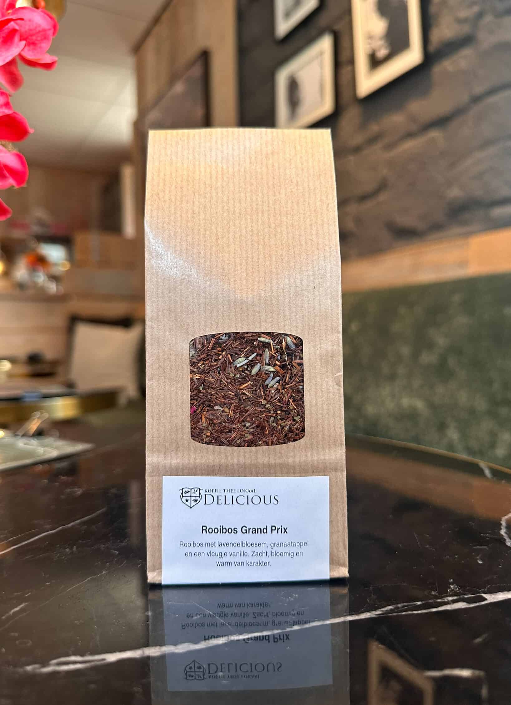 Rooibos Thee in een papieren verpakking met label, gelegen op een tafel in Koffie Thee Lokaal Delicious, met een rustieke achtergrond en muurdecoraties.