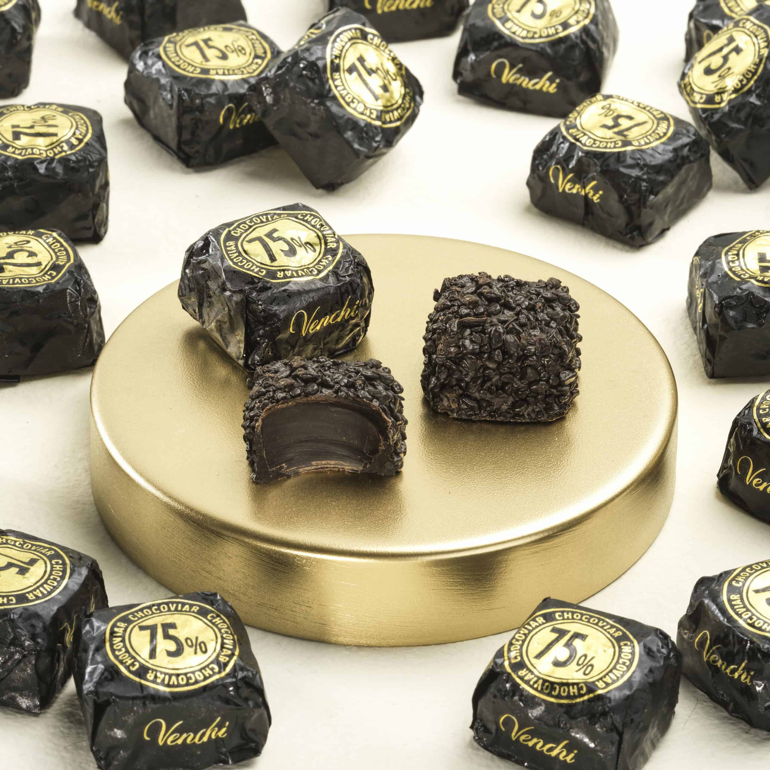 Zwarte Venchi chocolade truffels met 75% cacao, gepresenteerd op een goudkleurige schaal, omringd door meer chocolade truffels in hun zwarte verpakkingen, perfect voor chocolade- en koffieliefhebbers.