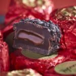Luxe chocolade truffel met karamelvulling, omgeven door rood verpakkingspapier, perfect voor koffie en thee liefhebbers bij Koffie Thee Lokaal Delicious.