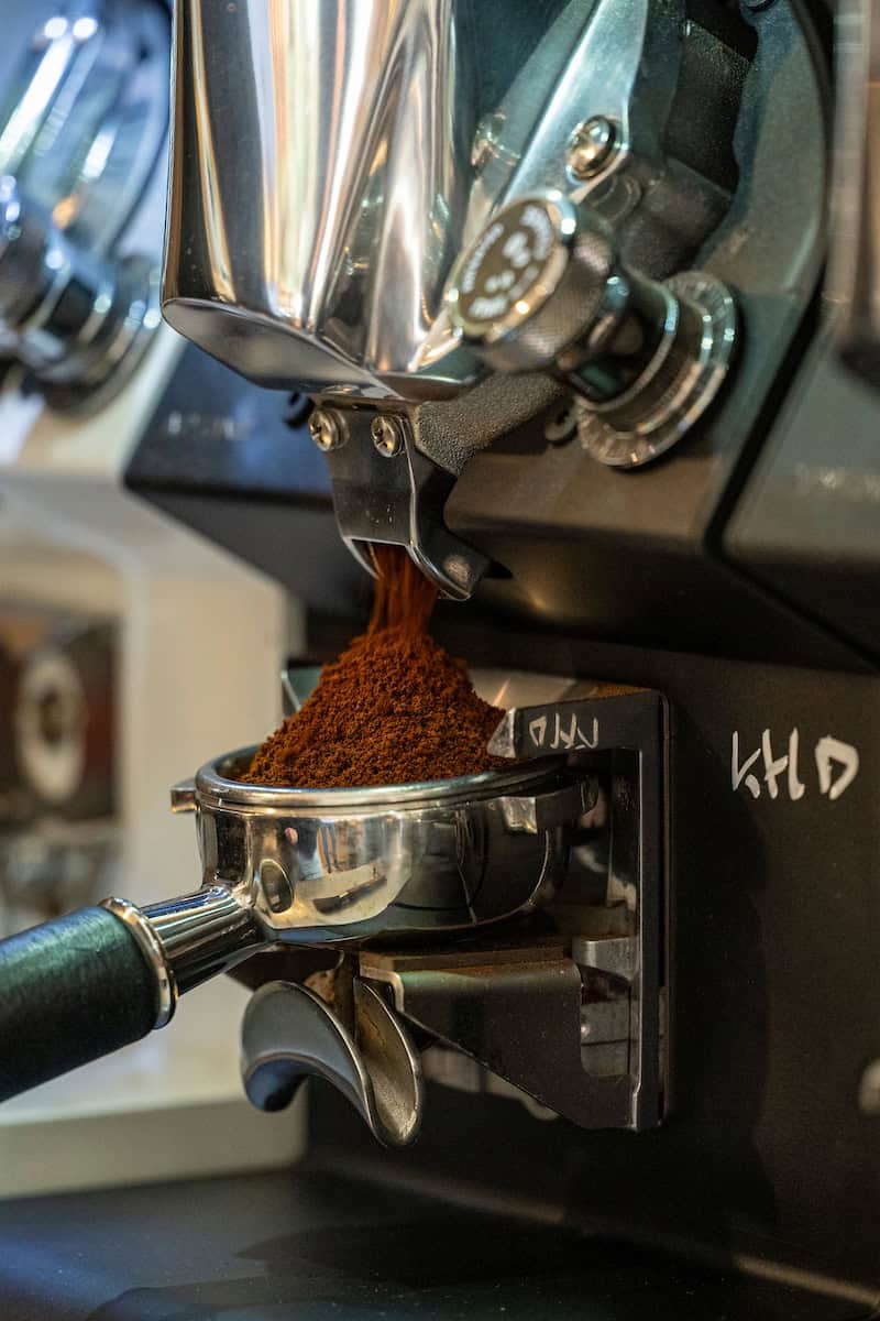 Espressomachine die gemalen koffie in een portafilter maalt, klaar voor het zetten van verse koffie bij Koffie Thee Lokaal Delicious. Perfect voor koffieliefhebbers die genieten van hoogwaardige koffi.